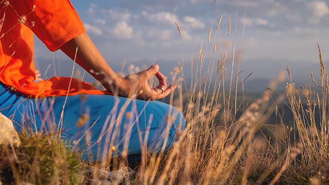 Unidentified woman meditates in lotus position on a grassy hill