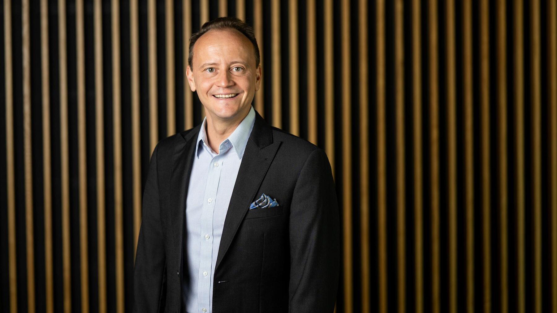 Man in a suit jacket stands in front of a striped wall.