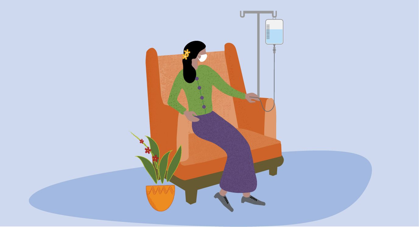 masked woman wearing green sweater and purple skirt sitting in clinic receiving IV chemotherapy with a flowering plant sitting on the floor beside her chair