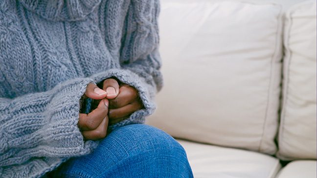 Black woman fidgeting with her fingers while sitting on the couch