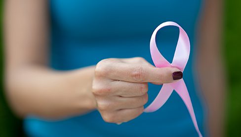 Hand holding pink ribbon symbolizing breast cancer