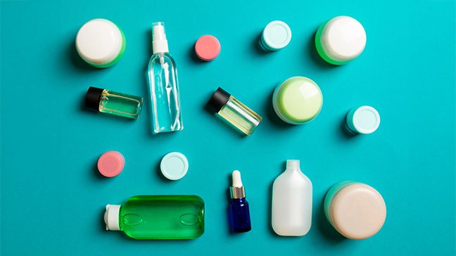 Flat lay image of multicolored personal care and beauty product packaging against a teal background