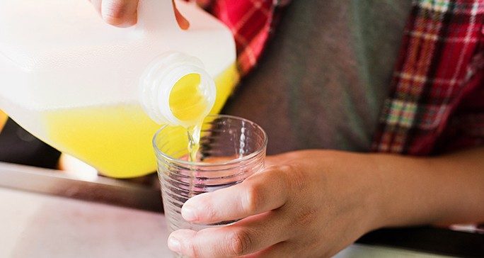 Person in plaid shirt pours a gallon of yellow liquid into a clear glass