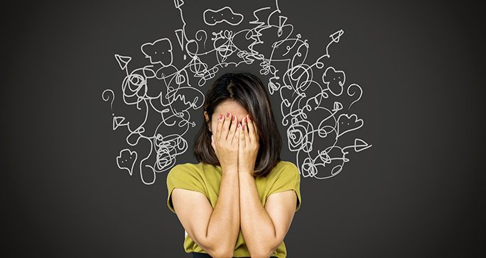 Women in green shirt holds her face in her hands. Doodles of white arrows, speech bubbles and question marks are frame her head.