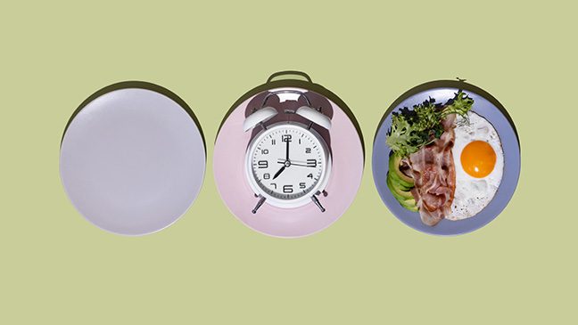 Three plates sit on a green surface. On the left, there is an empty purple plate. In the middle, there is a pink plate holding a white alarm clock. On the right, there is a blue plate with greens, bacon and a fried egg.