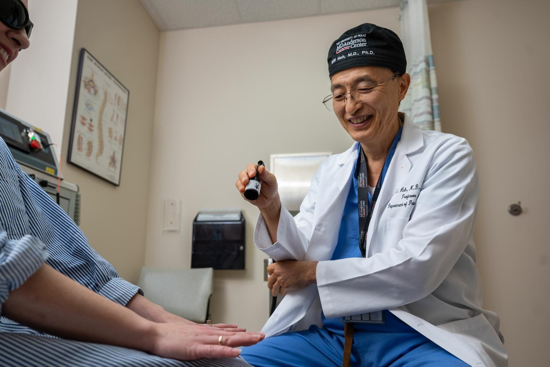 Pain management specialist Billy Huh, M.D., Ph.D., demonstrates using red light therapy for peripheral neuropathy on a person's hands.