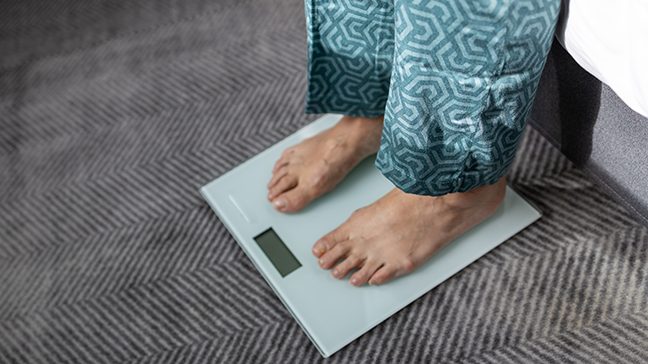 Older woman wearing pajamas stands on a scale