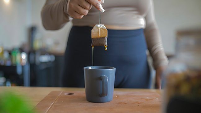 Woman holds a tea bag over a mug of hot water