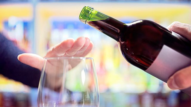 Person places their hand over an empty wine glass as someone starts to pour from a wine bottle