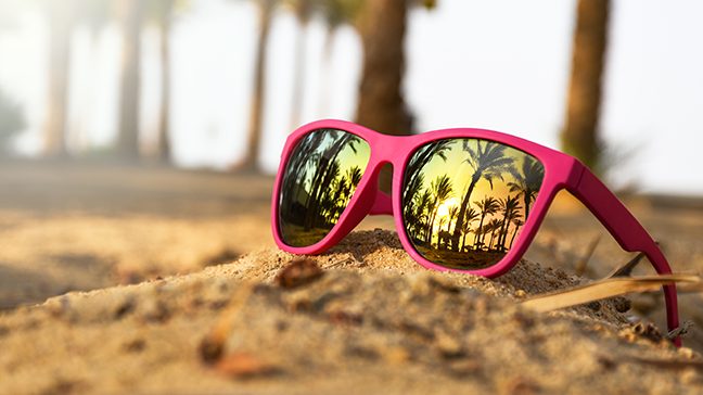 Close-up view of hot pink sunglasses with mirrored lenses on beach sand