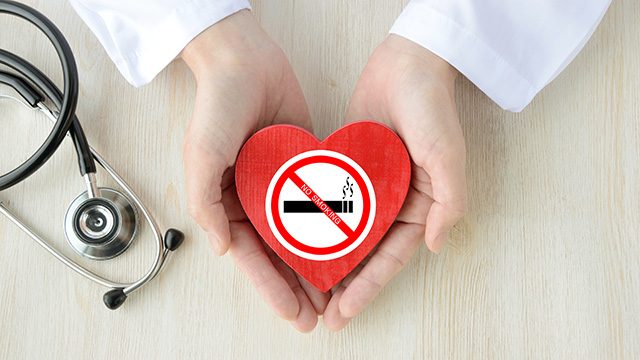 Close-up of a doctor's hands cupping a red paper heart with a no-smoking icon on it
