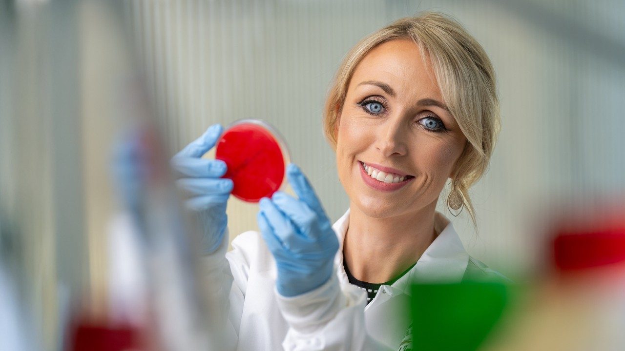 Dr. Bullman holds a petri dish up to camera while smiling